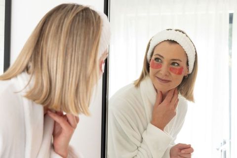 Midlife woman practicing skincare with under-eye gel patches at vanity mirror