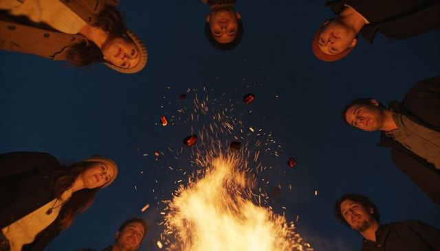 Friends gathering around bonfire at night with flying sparks and warm firelight