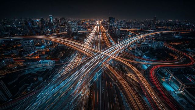 Glowing X-shaped highway interchange forming light trails over neon-lit cityscape at night