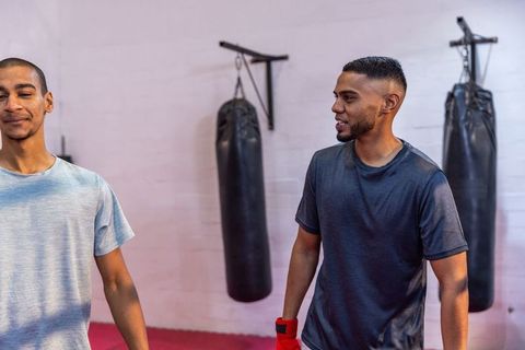 Male training partners talking in boxing gym with punching bags and red hand wraps