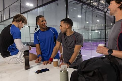 Group of men chatting and resting at indoor glass racquet court with purple surface