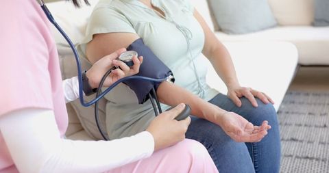 Nurse measuring blood pressure of senior woman during home visit