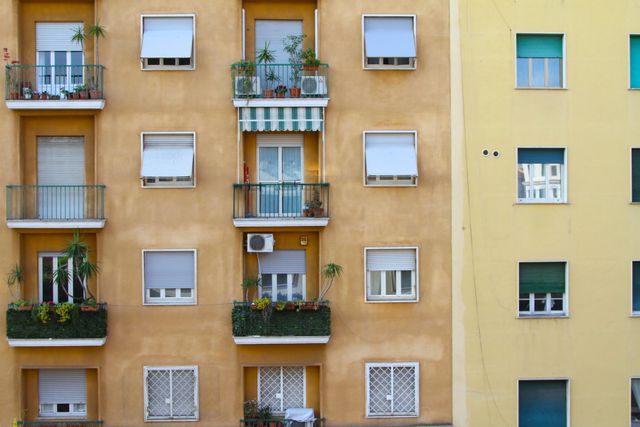 The image shows the exterior of a colorful apartment building with a variety of balconies. Each balcony features different plants and decorations, providing a personalized touch to the urban residence. This photo is perfect for use in real estate advertisements, articles on urban living, architecture presentations, or for decorating urban-themed interior spaces.
