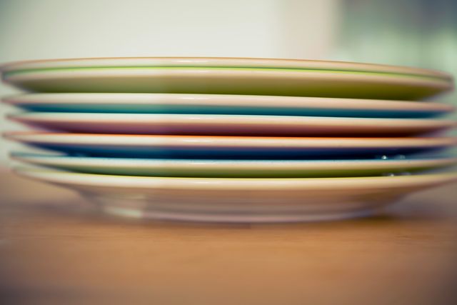 Close-up of stacked colorful plates on a wooden table, perfect for themes of kitchen decor, dining, and home organization. Could be used in advertisements for cookware, home goods, or restaurant supplies.