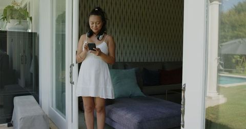 Smiling woman in white dress standing by open patio door on sunny day