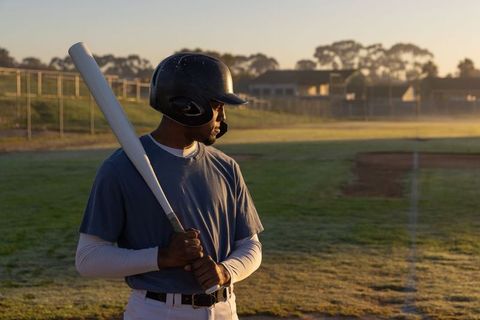 African American baseball player standing ready at dawn holding bat on community field