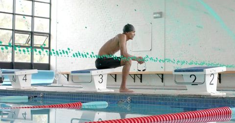 Competitive swimmer sitting on starting block 3 holding goggles at indoor lap pool