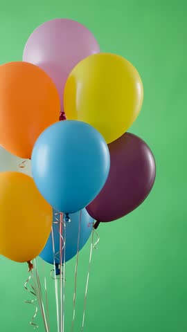 Vertical video showing stabilizing cluster of colorful balloons swaying against green wall
