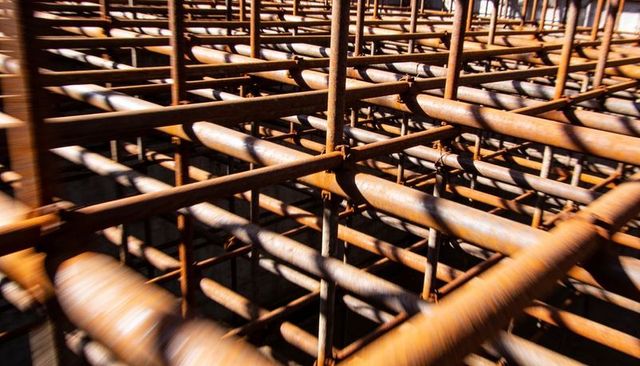 Rusted rebar grid forming geometric cage with strong lines, patina texture, shadows