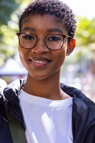 Confident african woman smiling in glasses on sunny urban street wearing jacket with bag