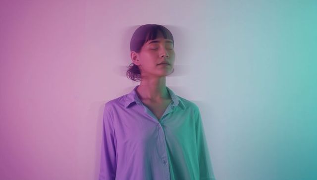 Standing woman wearing shirt facing wall with pastel pink-to-teal gradient and ghosting