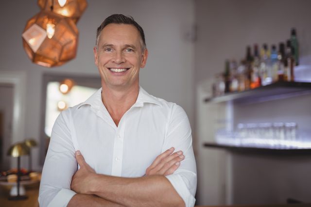 Portrait of happy man standing with arms crossed in restaurant