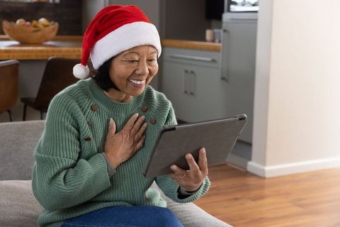 Senior woman in santa hat video calling with tablet during holidays