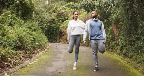 Young couple stretching and balancing on mossy forest trail wearing hoodies and headphones