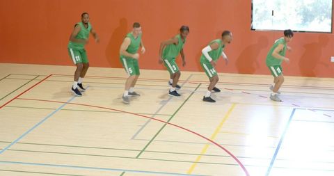 Diverse male basketball team warming up on indoor court practicing dynamic footwork