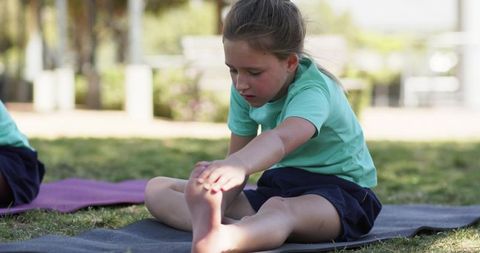 School girls stretching on yoga mats outdoors reaching forward for toe touch exercise