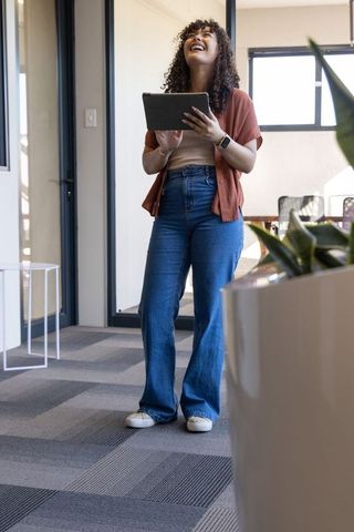 Laughing african american woman holding tablet and looking up in modern office corridor
