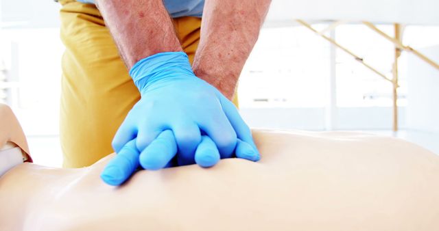 Medical professional wearing blue gloves performing CPR chest compressions on a training mannequin. Suitable for use in healthcare training, first aid courses, emergency preparedness materials, and educational resources related to life-saving techniques.