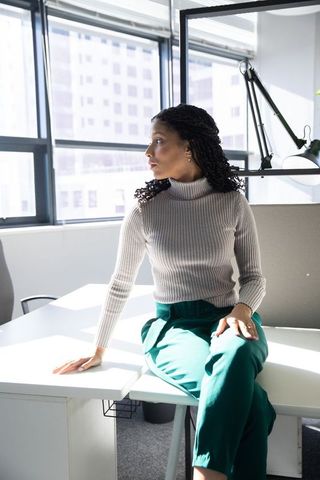 African american woman sitting on desk looking out window in modern minimalist office