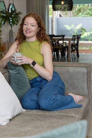 Red-haired woman relaxing on suede sofa sipping coffee in cozy modern living room