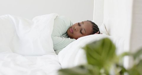 African american woman resting on white bedding in minimalist bedroom with indoor plant