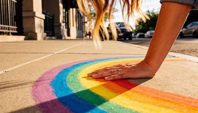 Pressing hand onto vibrant rainbow chalk on city sidewalk, urban street art close-up