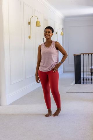Smiling black woman standing barefoot in bright hallway wearing pink top and red leggings
