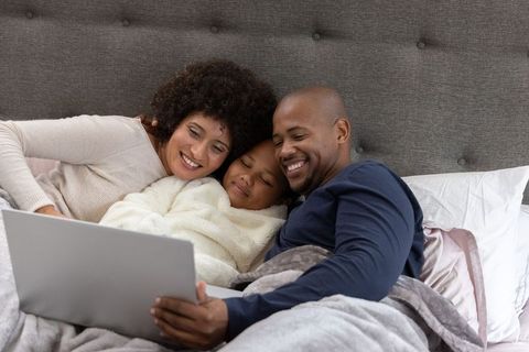 Cozy morning family streaming together in bed, parents cuddling child with laptop