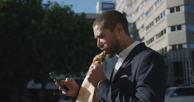 Businessman enjoying a quick takeaway meal while checking his smartphone in a bustling urban environment. Ideal for illustrating modern lifestyles, busy professionals, time management, productivity, and work-life balance. Suitable for use in articles, advertisements, and promotions related to business, technology, and urban living.