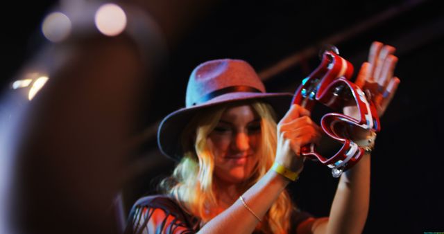 A young Caucasian woman is enjoying a music festival, playing with a colorful tambourine, with copy space. Her joyful expression and casual festival attire capture the vibrant atmosphere of the event.