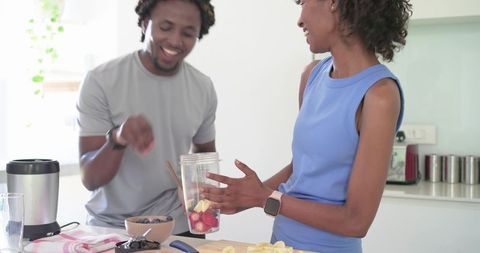 African american couple making fresh berry smoothie in bright modern kitchen