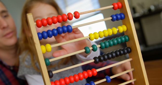 Father and daughter are using a colorful abacus. Adult and child bonding together while learning basic math concepts. Perfect for educational material, parenting articles, and family-related content.