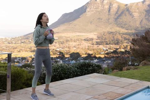 Asian woman standing holding kettlebell on poolside patio with mountain view