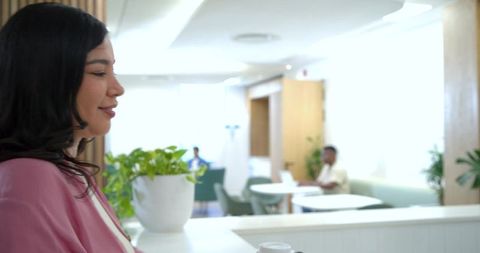 Young woman leaning on counter in modern office lounge with coffee cup, sunlit coworking