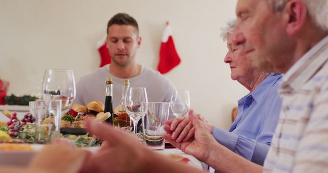 Caucasian family having christmas dinner. sitting on dining table holding hands and praying together before having lunch during christmas at home. christmas festivity celebration tradition