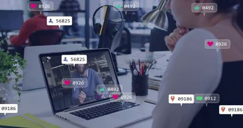 Woman watching virtual meeting on laptop in modern coworking office with social reactions
