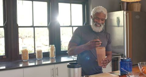 Senior man mixing nutritional shake in modern kitchen
