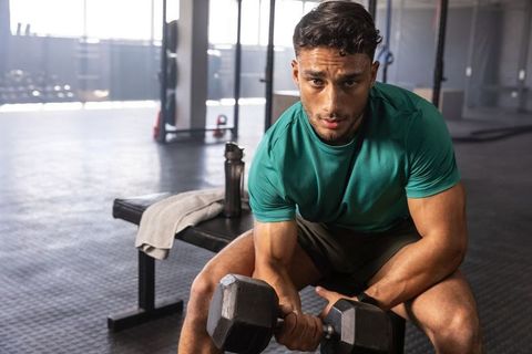 Focused muscular man performing seated dumbbell curl on bench in gym, strength training