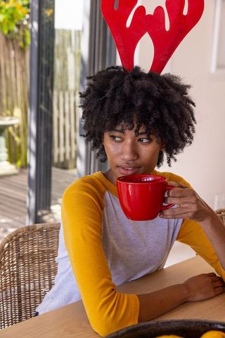 Festive woman drinking hot beverage at home inside