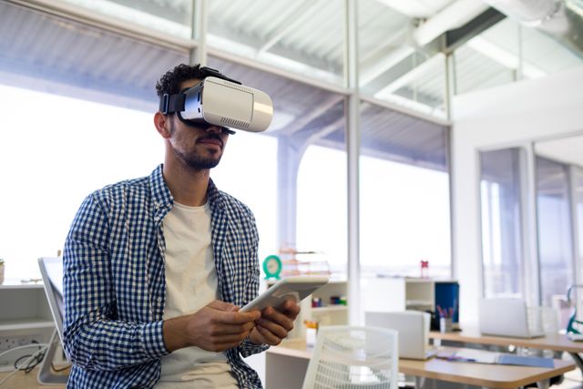 Male executive using virtual reality headset and digital tablet in office