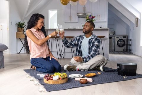 Couple toasting on knit indoor picnic blanket in loft kitchen with charcuterie platter