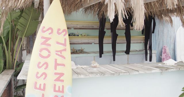 Tropical surf shop featuring surfboard rentals and wetsuits hanging from racks. Ideal for marketing materials related to beach vacations, surfing tutorials, or coastal sports lifestyle. Great for use in travel blogs, social media posts, or brochures promoting water activities.