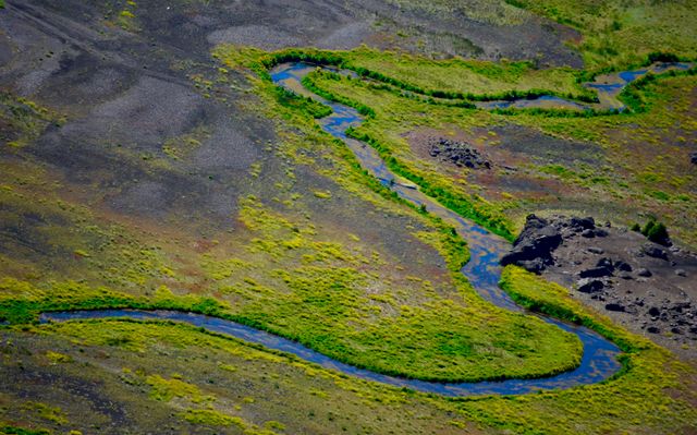 A winding river snakes through verdant greenery, offering a striking contrast to the surrounding terrain. Ideal for use in environmental science presentations, landscape photography collections, travel brochures, and educational materials highlighting natural formations and waterways.
