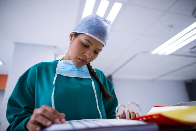 Female surgeon in surgical attire reviewing medical reports in a hospital operating room. Ideal for use in medical, healthcare, and hospital-related content, showcasing professionalism and dedication in the medical field.
