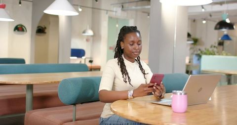 African American woman working in modern coworking space using smartphone and laptop