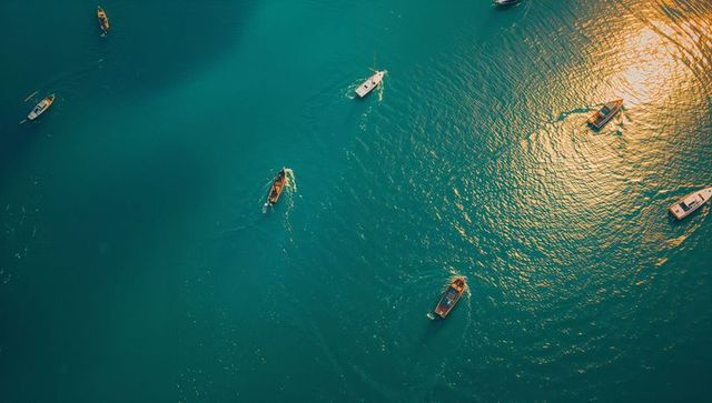 Sunlit teal bay with boats gliding and leaving wake trails — aerial seascape