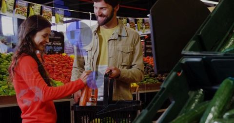 Couple placing carrots into basket while grocery shopping fresh produce at market