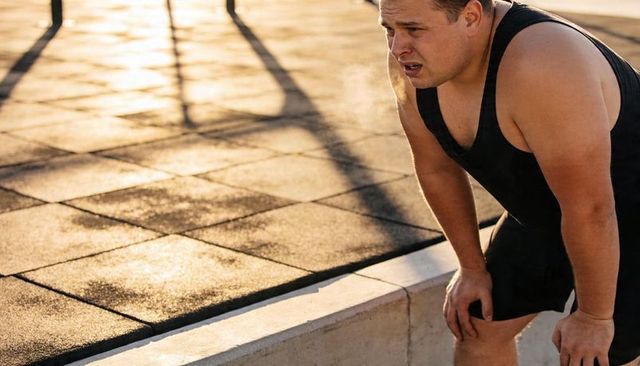 Man leaning on curb after workout breathing cold air at sunset fitness recovery outdoor park