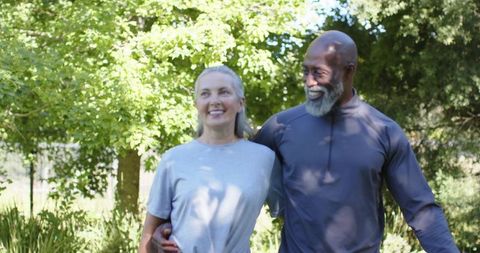 Mature couple walking under dappled sunlight, smiling and embracing on leafy park stroll