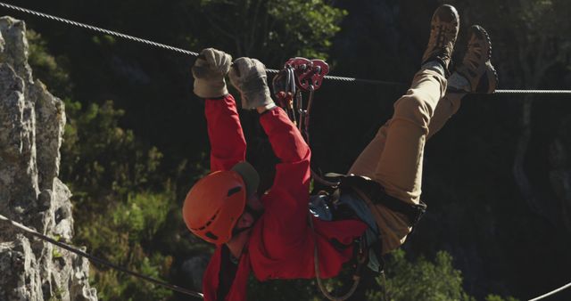 Adventurer wearing safety gear hanging from zip line over valley, engaged in exciting extreme sport. Perfect for outdoor adventure advertisements, travel brochures, extreme sports magazines, or safety gear promotions.
